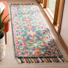 a colorful runner rug with tassels on the floor next to a potted plant