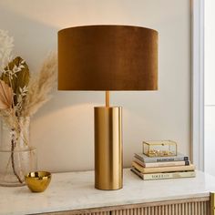 a gold lamp sitting on top of a white table next to a vase with flowers