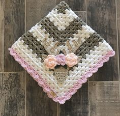 a crocheted blanket with flowers on it sitting on a wooden floor next to a pair of scissors