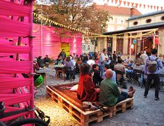 many people are sitting on wooden benches in the middle of an outdoor area with pink lanterns