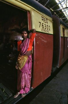 a woman standing on the side of a train at a station with her arms behind her head