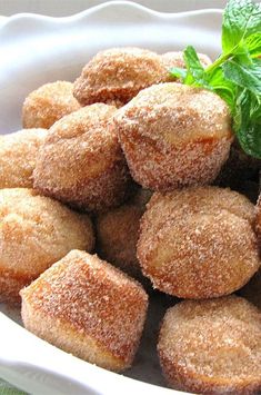 a white bowl filled with sugared pastries covered in green leaves