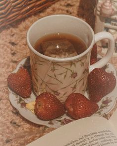 a cup of tea with strawberries on a saucer next to an open book