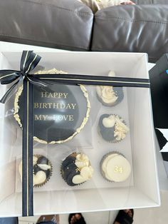 a box filled with lots of cupcakes on top of a table next to a person's feet