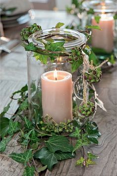 a candle that is sitting inside of a glass jar with greenery on the table