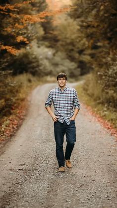 a man standing in the middle of a dirt road with trees around him and his hands on his hips