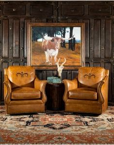 two brown leather chairs sitting in front of a painting