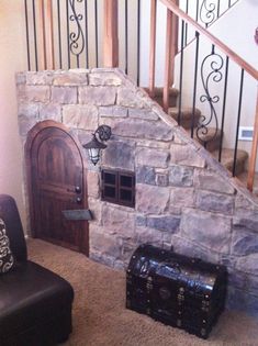 a living room with a stone wall and stair case next to a leather ottoman in front of a wooden door