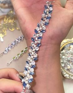 a woman is holding onto a bracelet with blue and white crystals on it, while another watch sits in the background