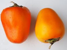 two orange tomatoes sitting next to each other on a white surface