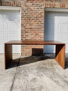 a wooden table sitting in front of a brick building with two garage doors behind it