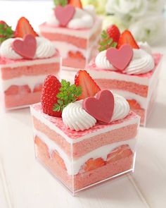 four pieces of cake with strawberries and hearts on top, sitting on a table