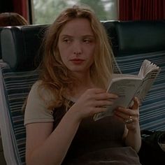 a woman reading a book while sitting on a train seat with her eyes closed and looking down