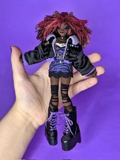 a hand is holding a doll with red hair and black clothes on it's body