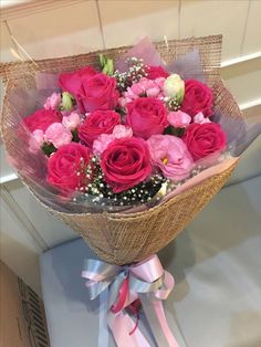 a bouquet of pink and white roses in a wrapper on a table with ribbon