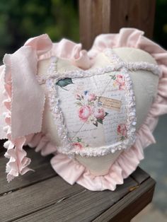 a white heart pillow with pink ruffles on it sitting on top of a wooden bench