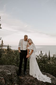 a bride and groom standing on top of a mountain looking at the camera with an ocean in the background