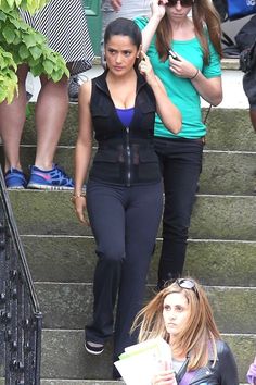 two women are walking down the stairs talking on their cell phones and one is holding a magazine