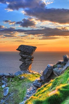 the sun is setting over an ocean with rocks and grass on the side of it