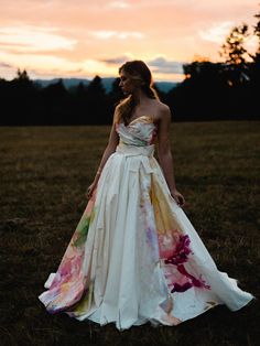 a woman standing in a field at sunset wearing a dress with flowers on the skirt