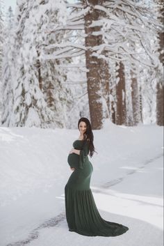 a pregnant woman standing in the snow wearing a long green dress and holding her belly