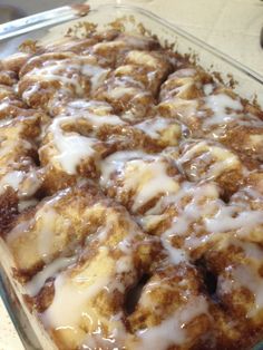 a glass baking dish filled with cinnamon rolls covered in icing and drizzle