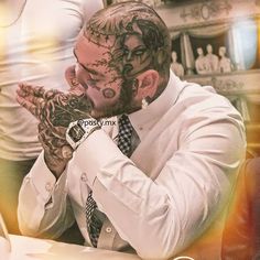 a man with tattoos on his face sitting at a table