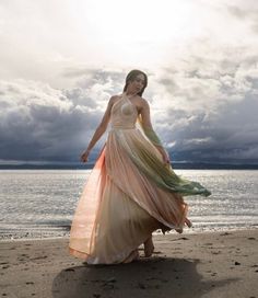 a woman in a long dress standing on the beach