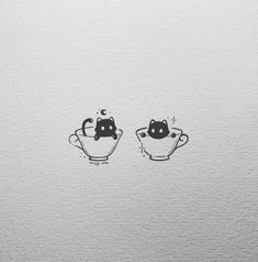 two cups with cats drawn on them sitting next to each other in front of a white wall