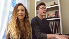 a man and woman sitting next to each other in front of a book shelf filled with books