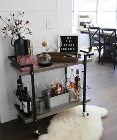 a bar cart with bottles and glasses on it next to a white sheepskin rug