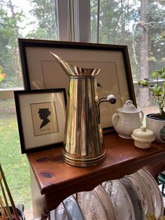 a gold pitcher sitting on top of a wooden table next to plates and vases