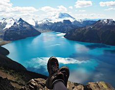 a person sitting on top of a mountain with their feet in the air looking out over a lake