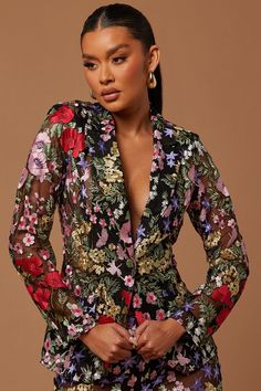 a woman wearing a floral print dress and gold earrings, standing in front of a brown background