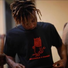 a man with dreadlocks looking at his cell phone while wearing a t - shirt