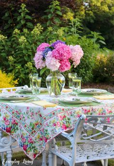 the table is set with flowers in vases and plates on it, along with glasses