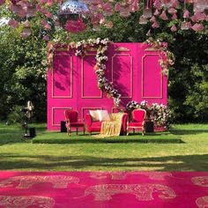 an outdoor ceremony setup with pink walls and red chairs, decorated with floral garlands