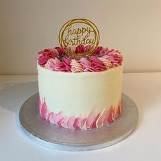 a birthday cake decorated with pink flowers and a gold happy birthday topper on a silver platter