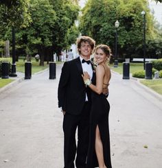 a young man and woman dressed in formal wear posing for a photo on the street