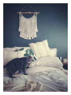 a cat sitting on top of a white bed next to pillows and a wall hanging