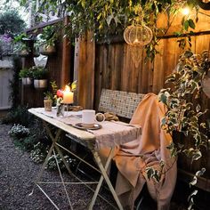 an outdoor table and chair with a blanket on it in front of a wooden fence