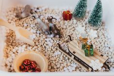 small christmas decorations in a white container with rocks and snow on the ground next to them