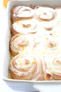 a white casserole dish filled with cinnamon rolls covered in icing and orange zest