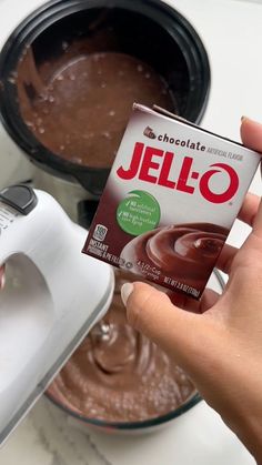 someone holding up a box of jello in front of a bowl of chocolate pudding