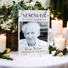 an old man is sitting in front of a memorial sign with flowers and candles around it