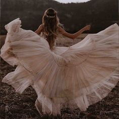 a woman in a white dress is walking through the grass with her arms spread out