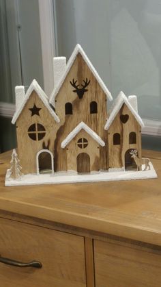 a small wooden house with trees and snow on the roof is sitting on top of a dresser