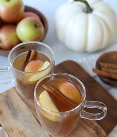 two mugs filled with apple cider on top of a wooden cutting board