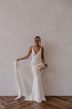 a woman in a white wedding dress holding a bridal bouquet and posing for the camera