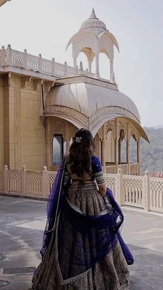 a woman in a blue and white dress is walking towards a building with an ornate roof